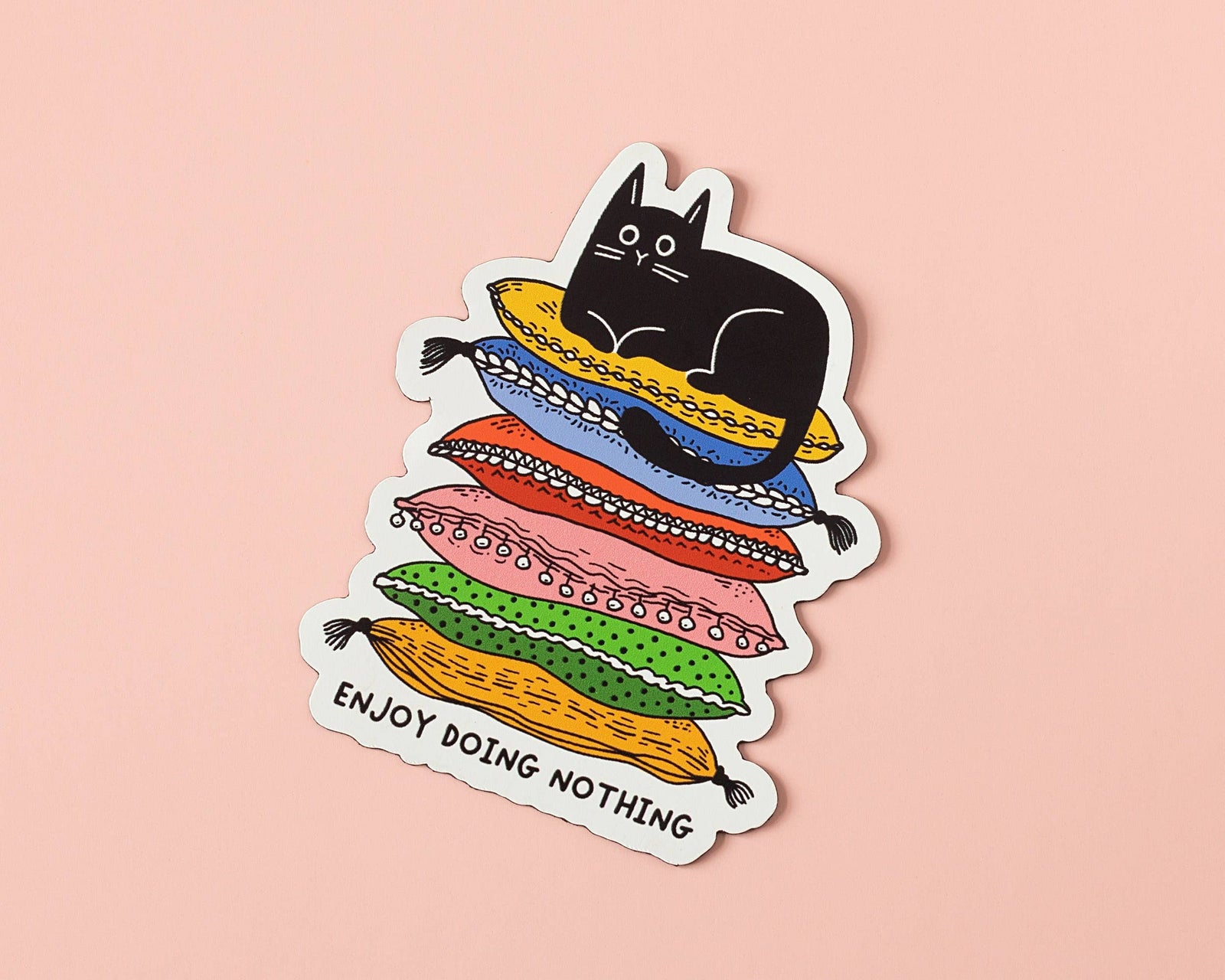 Sticker with a black cat on colorful cushions and 'Enjoy Doing Nothing' text on a pink background